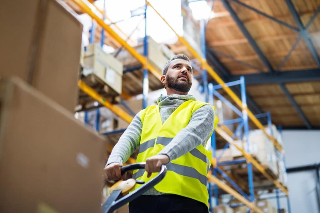 Warehouse worker pulling a pallet truck with boxes.