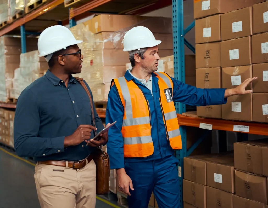 Male factory worker showing stock to his inventory using digital tablet in large warehouse